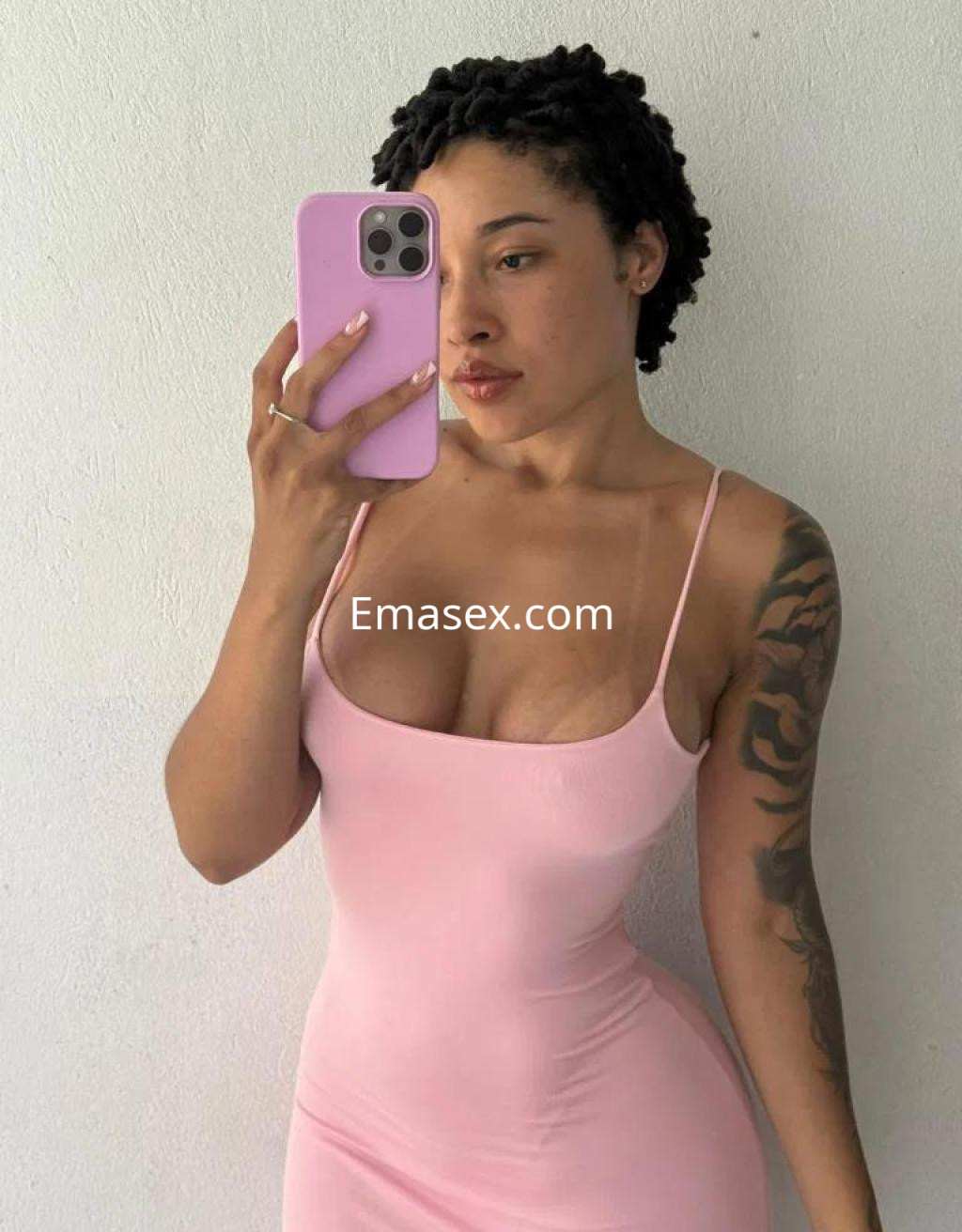 Escort en Málaga con cabello rizado, luciendo un vestido ajustado rosa y posando frente a un espejo.