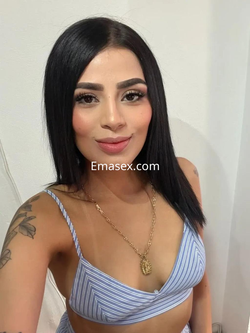 Escort en Murcia con cabello largo y lacio, viste un top de rayas y lleva un collar dorado, sonriendo a la cámara.