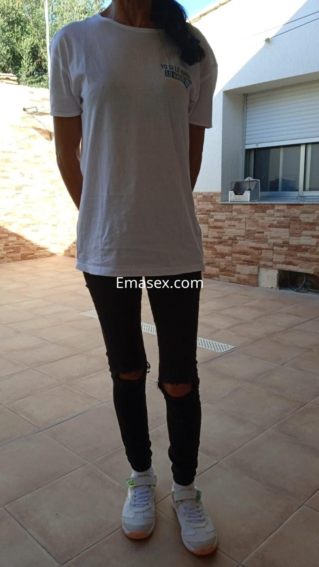 Escort en Murcia con camiseta blanca, jeans negros rasgados y zapatillas deportivas, posando en un entorno exterior.