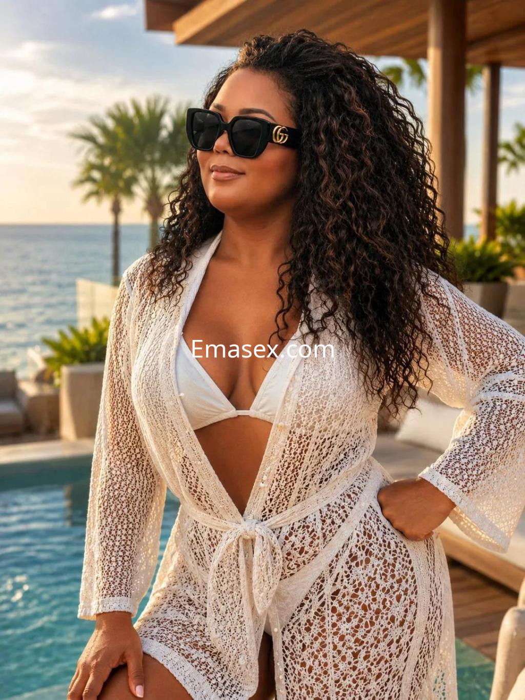 Escort en Gijón con cabello rizado y oscuro, vistiendo un conjunto blanco y gafas de sol, junto a una piscina.