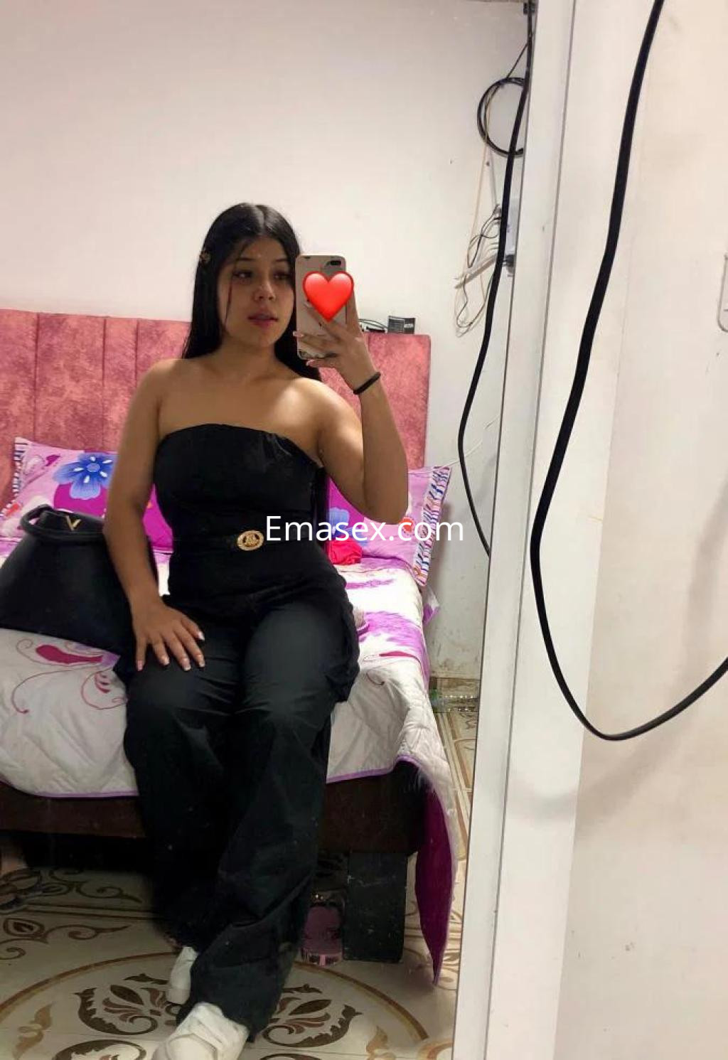 Escort en Las Palmas posando en un espejo, lleva un conjunto negro sin mangas y zapatillas blancas.