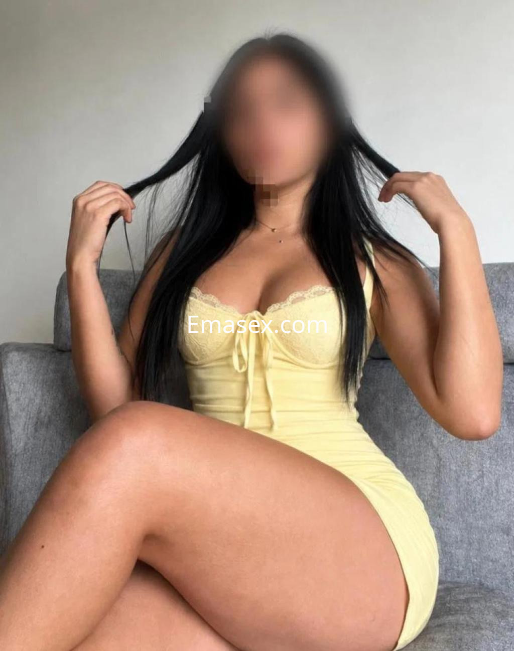 Puta en Las Palmas posa sentada en un sofá, luciendo un vestido amarillo ajustado y cabello largo y lacio.