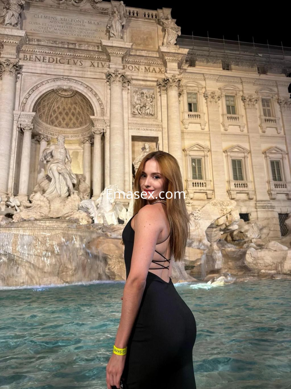 La puta posa de espaldas frente a la Fontana di Trevi en Valencia, luciendo un vestido negro elegante.