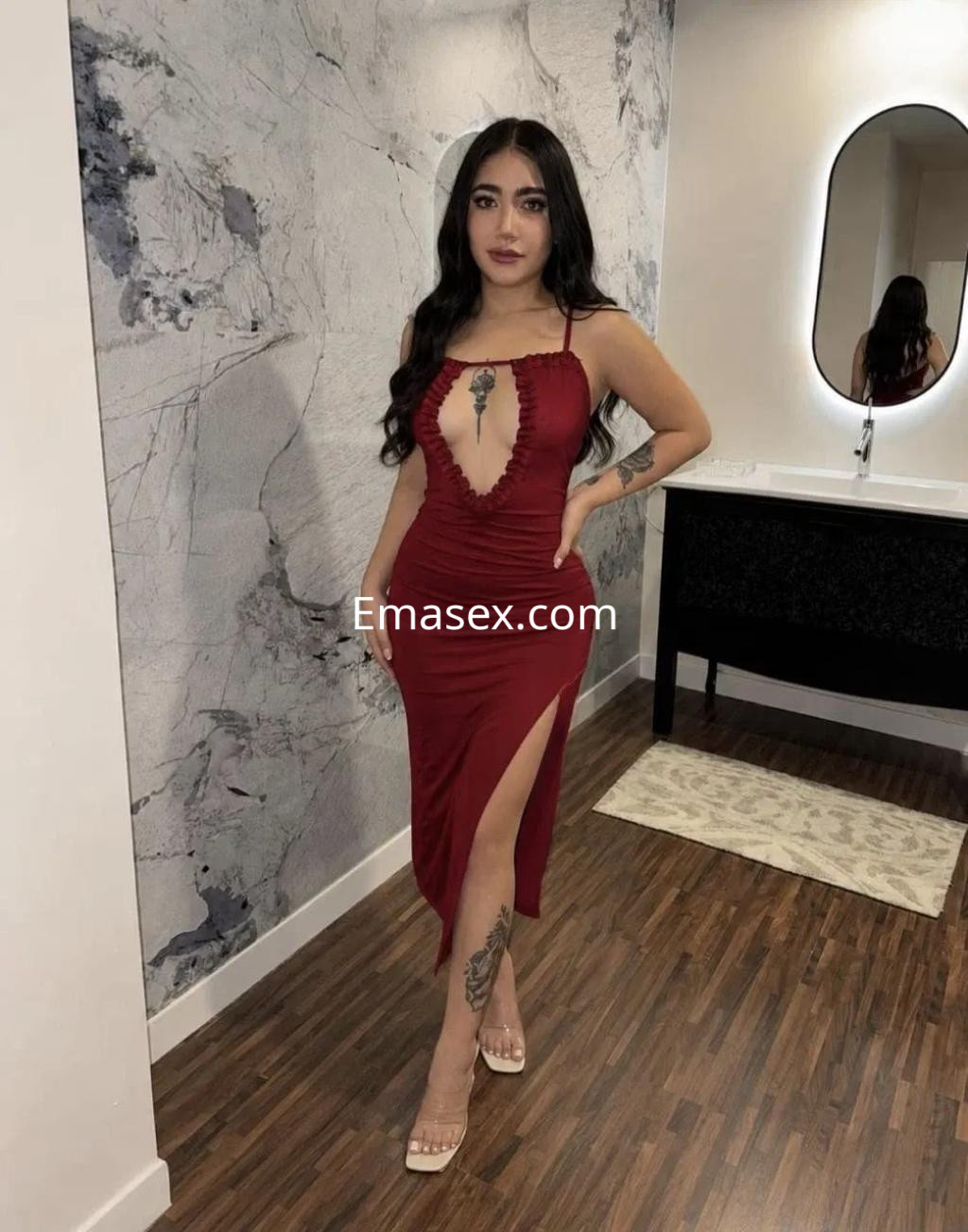 Escort en Zaragoza con cabello oscuro y lacio, luciendo un vestido rojo con escote y abertura lateral en un entorno moderno.