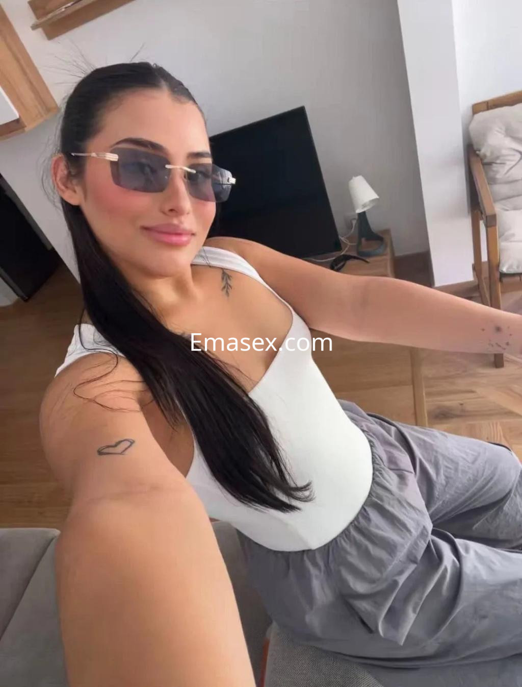 Escort en Zaragoza con cabello largo y lacio, usando gafas de sol y un conjunto de top blanco y pantalones grises.