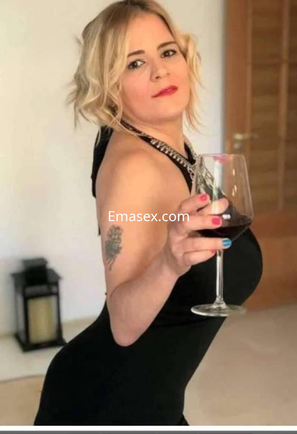 Puta en Zaragoza, luciendo un vestido negro ajustado mientras sostiene una copa de vino tinto con una pose seductora.
