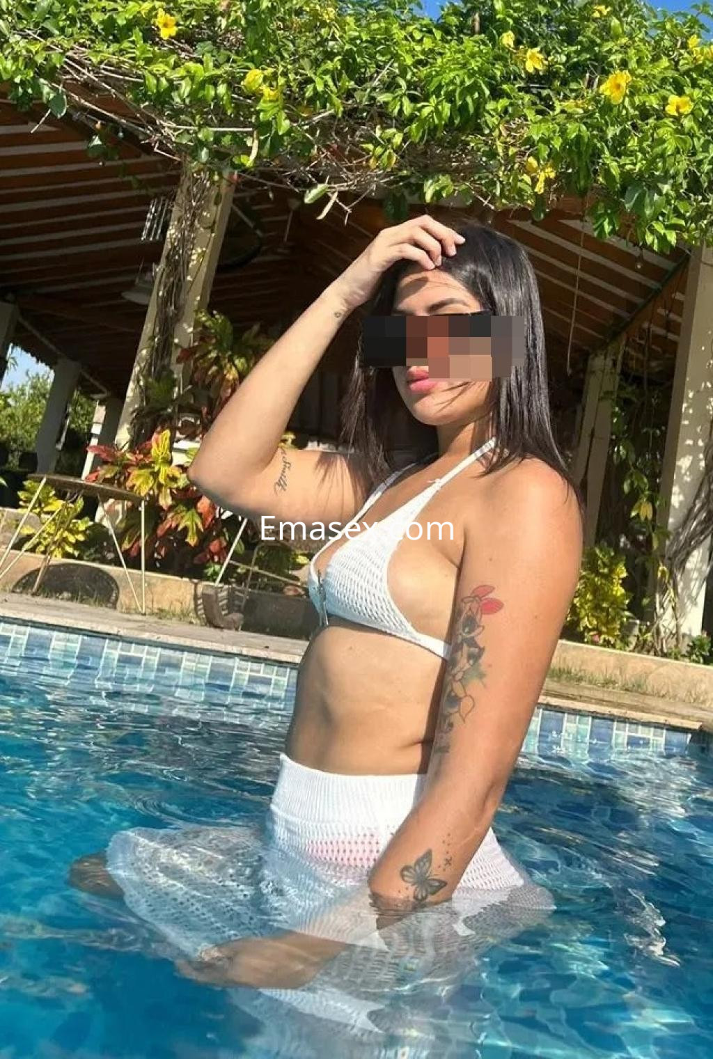 Escort en Gijón posando en una piscina, luciendo un bikini blanco y una falda de red, con cabello largo y oscuro.