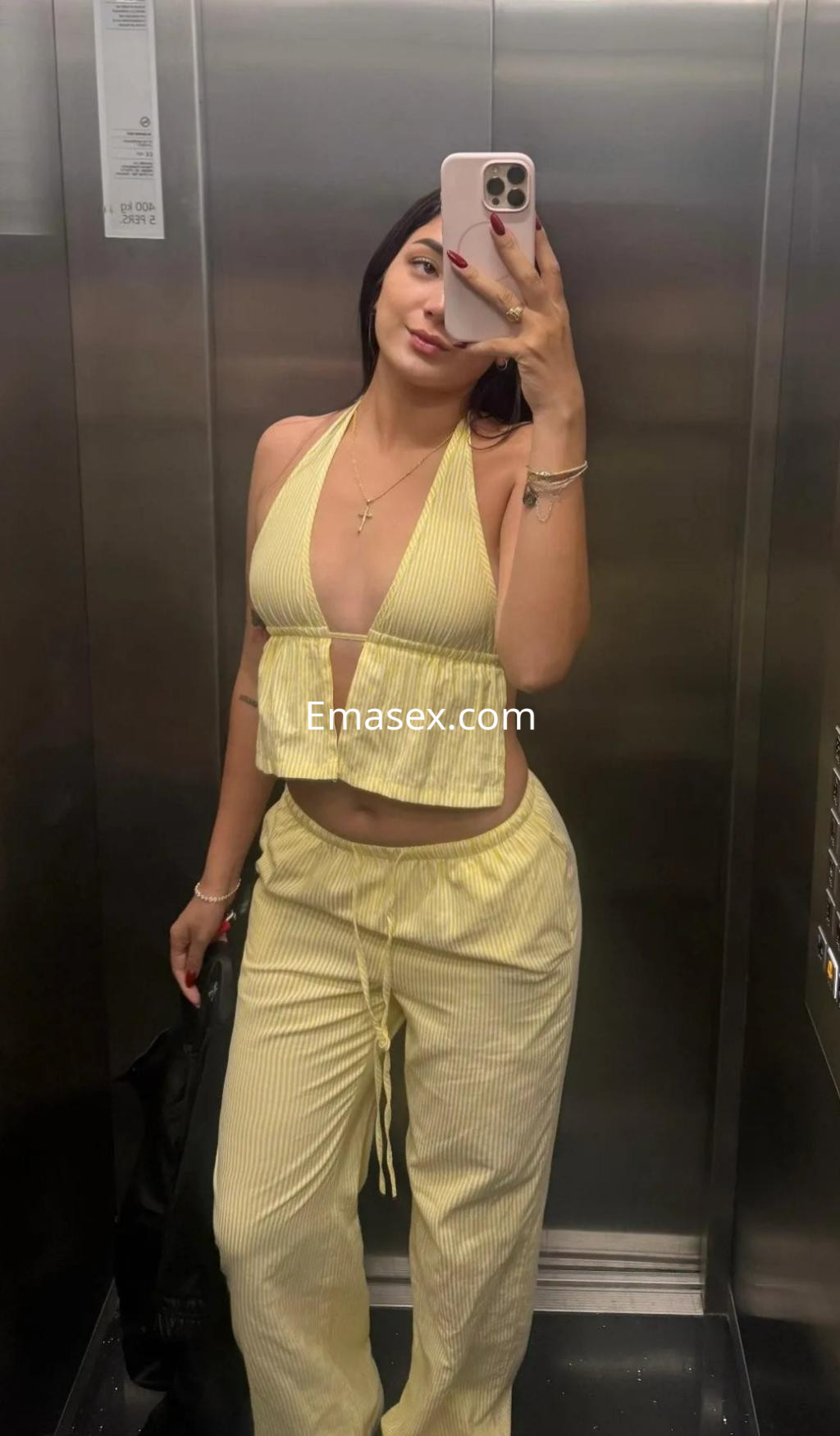Escort en Madrid posando en un ascensor con un conjunto amarillo de top halter y pantalones amplios.