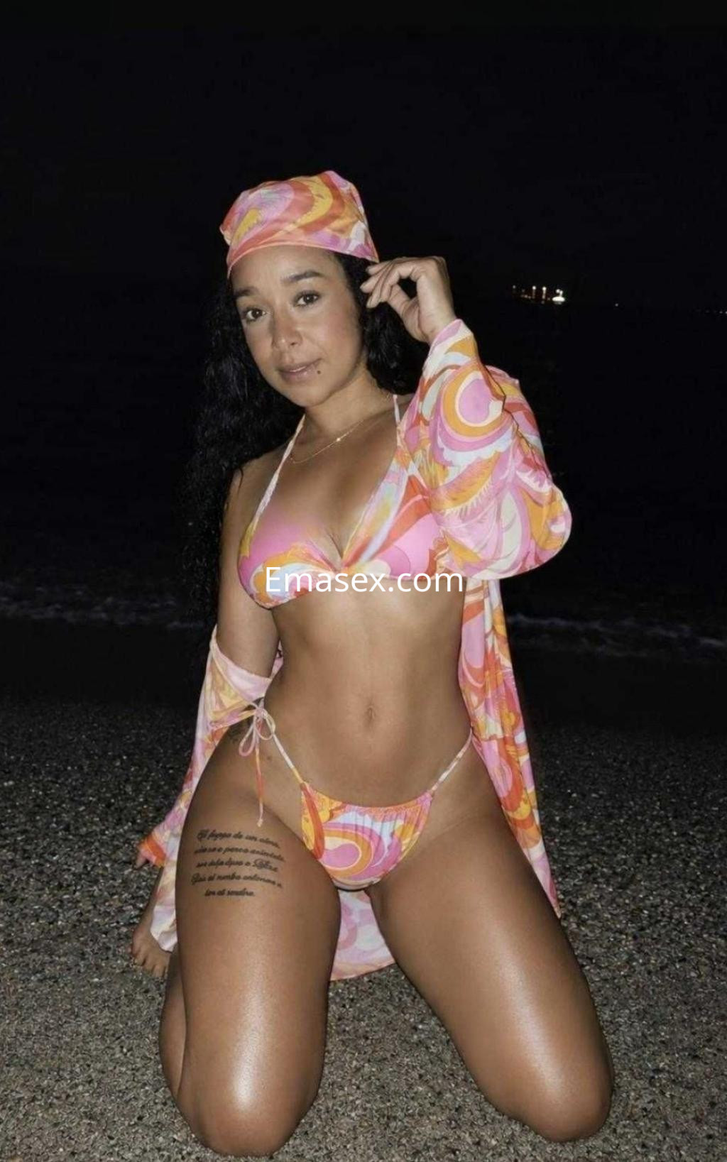 Puta posando en la playa de Barcelona, con bikini colorido y una camisa ligera, mostrando su piel bronceada.