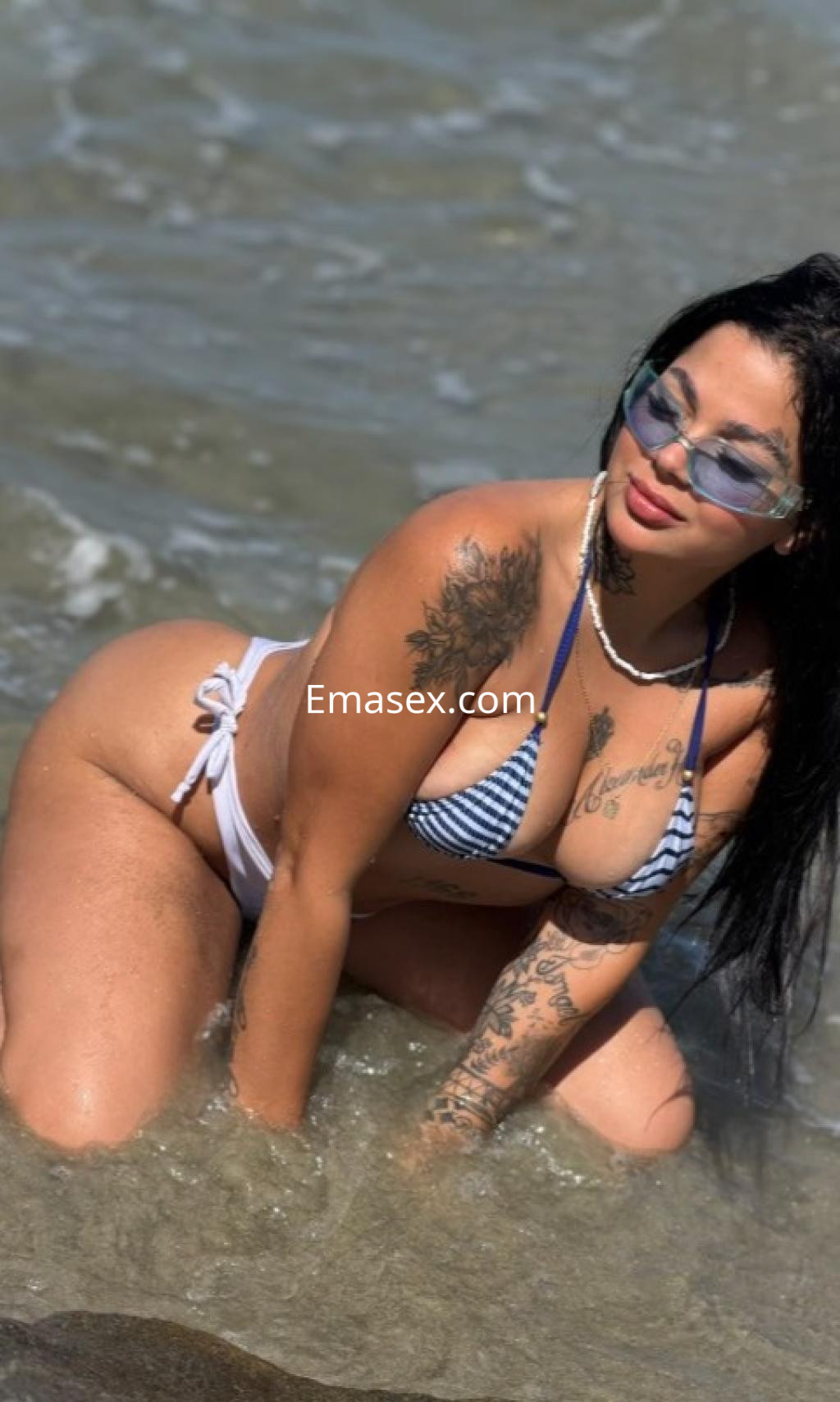 Puta en Valladolid, con cabello largo y oscuro, usando un bikini de rayas en la playa, posando en el agua.