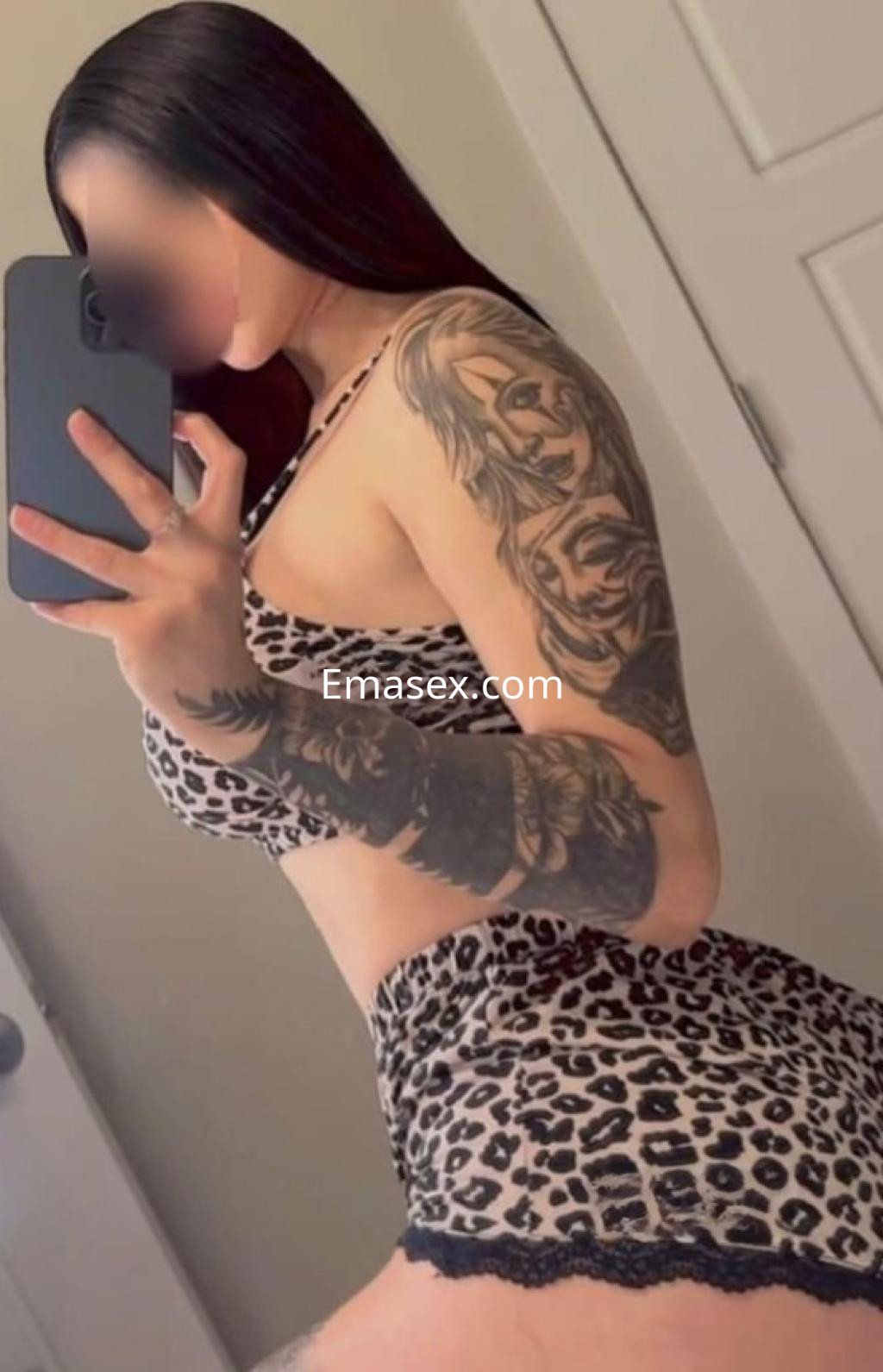 Escort en Valladolid con cabello oscuro, luciendo un conjunto de lencería de leopardo y tatuajes en el brazo.