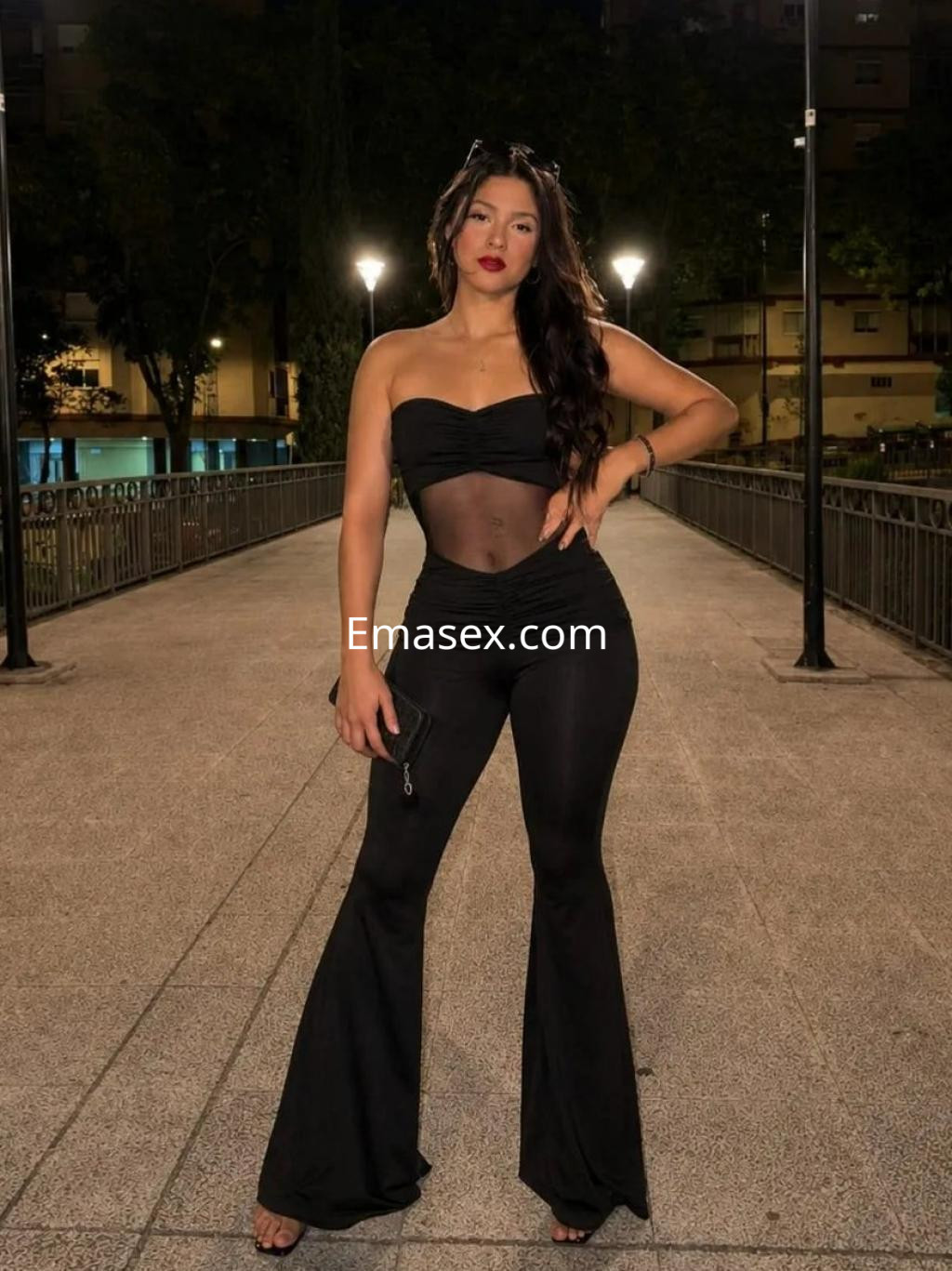 Escort en Zaragoza con un conjunto negro ajustado y transparencias, posando en un entorno urbano iluminado.