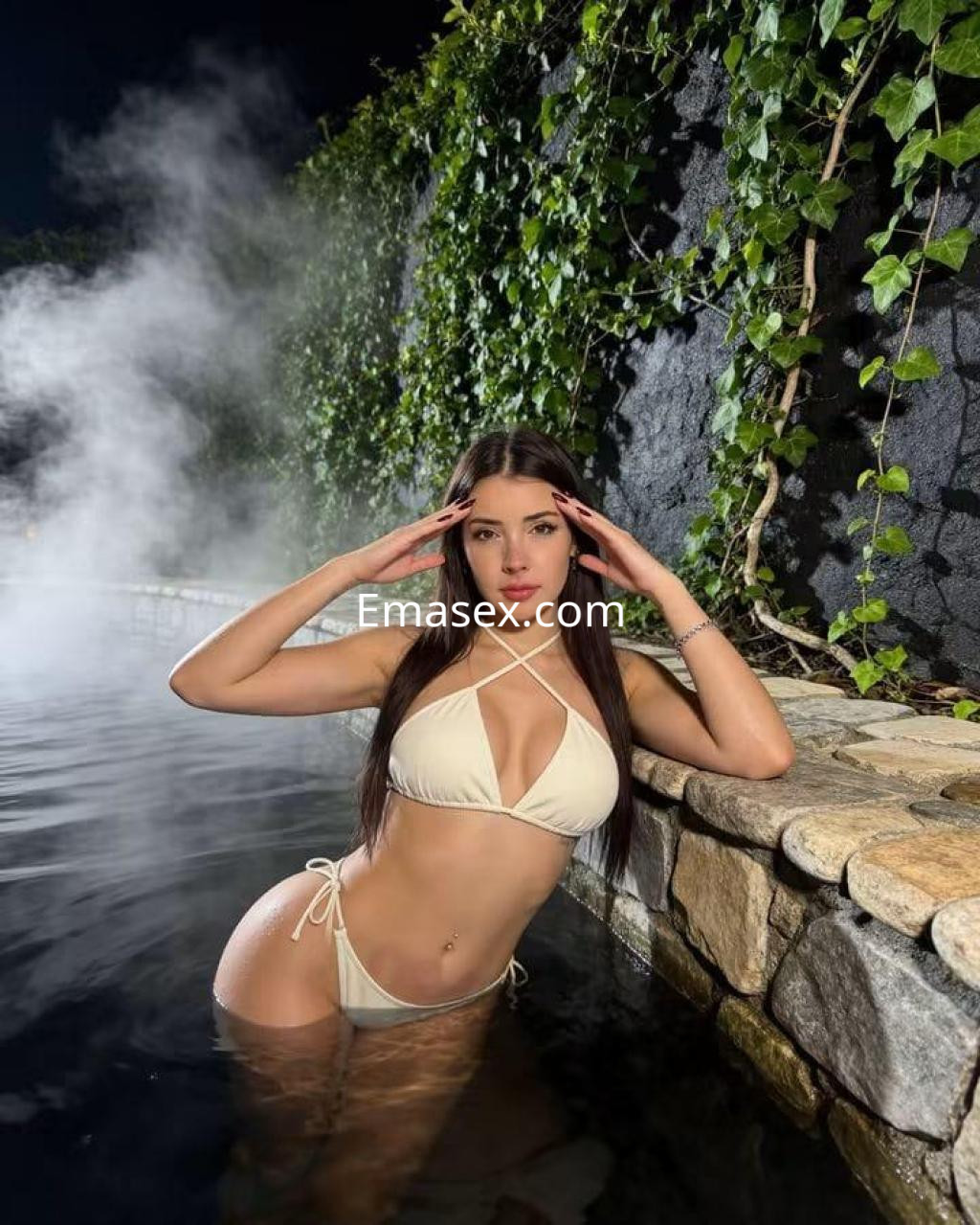 La puta luce un bikini blanco mientras posa en una piscina con vapor y plantas verdes en Málaga.