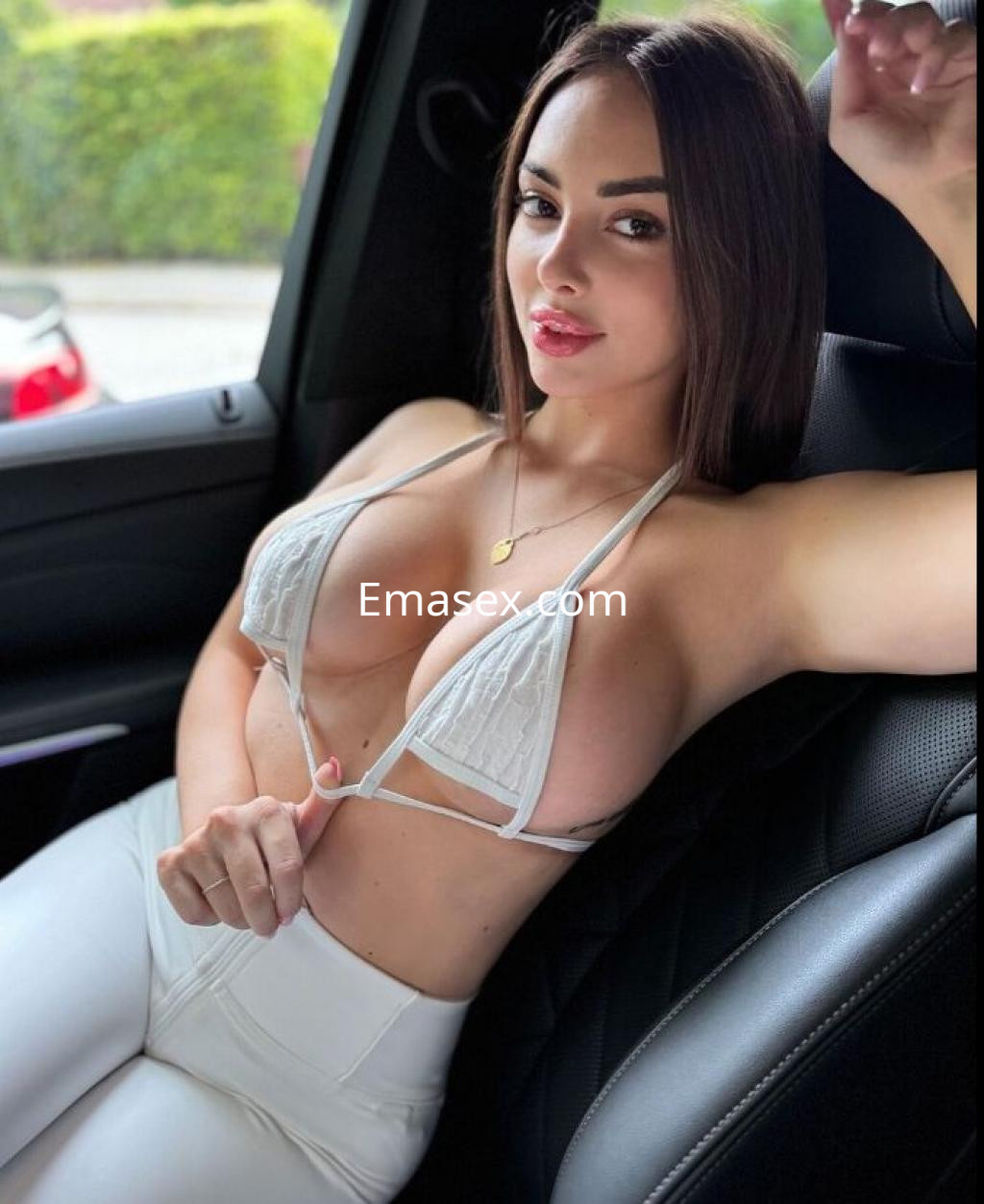 Escort en Pamplona con cabello castaño claro, luciendo un top blanco y pantalones ajustados, sentada en un coche.