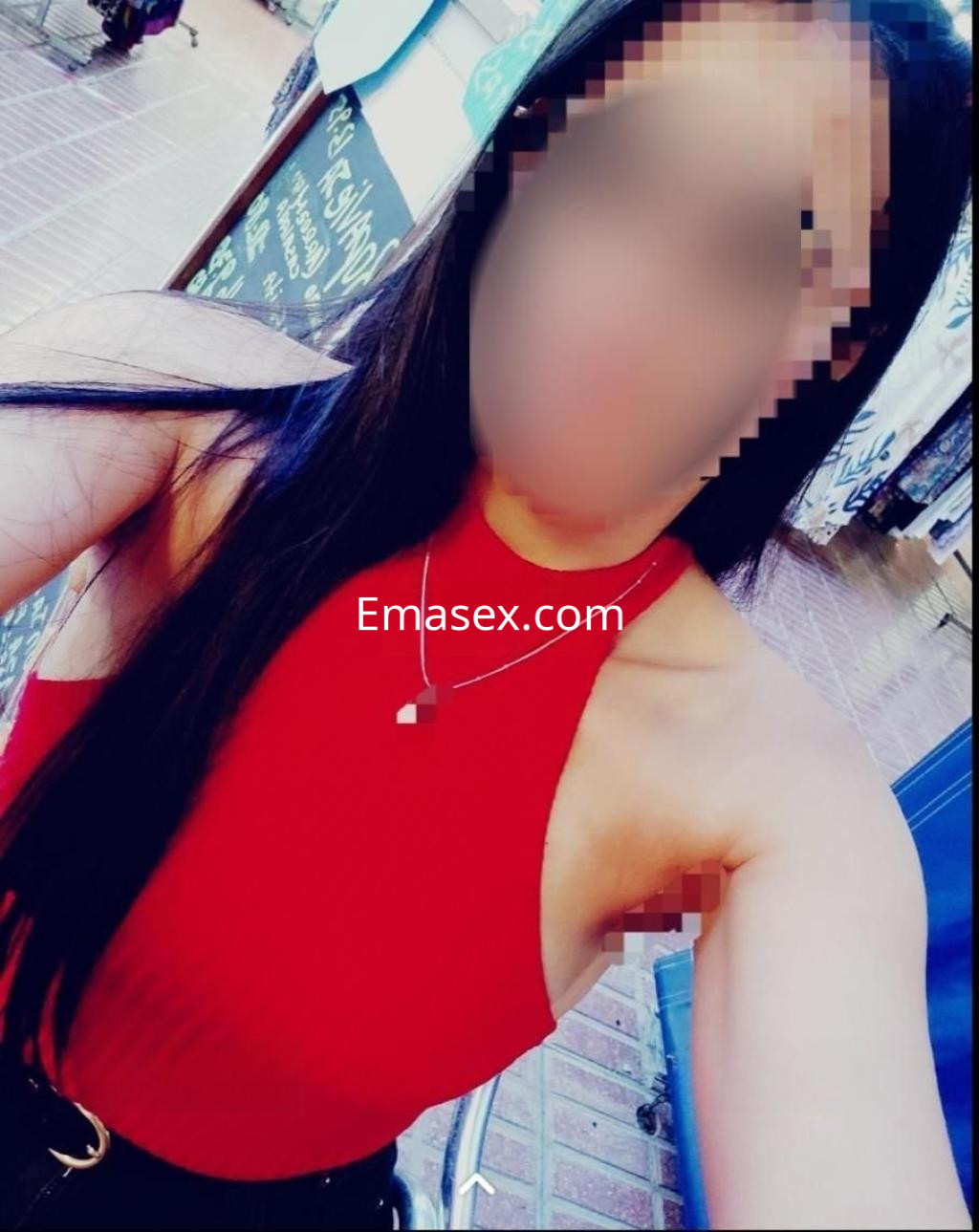 Puta con blusa roja ajustada y cabello largo, posando en un entorno urbano en Almería.