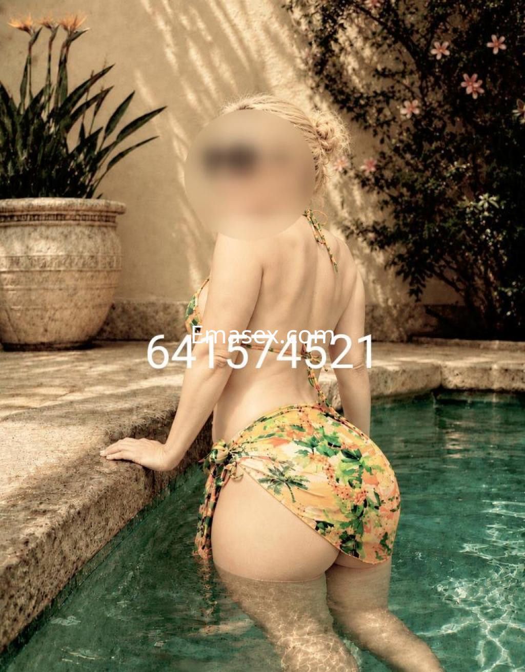 Puta en Badajoz, de espaldas en una piscina, luciendo un bikini floral y con el cabello trenzado.