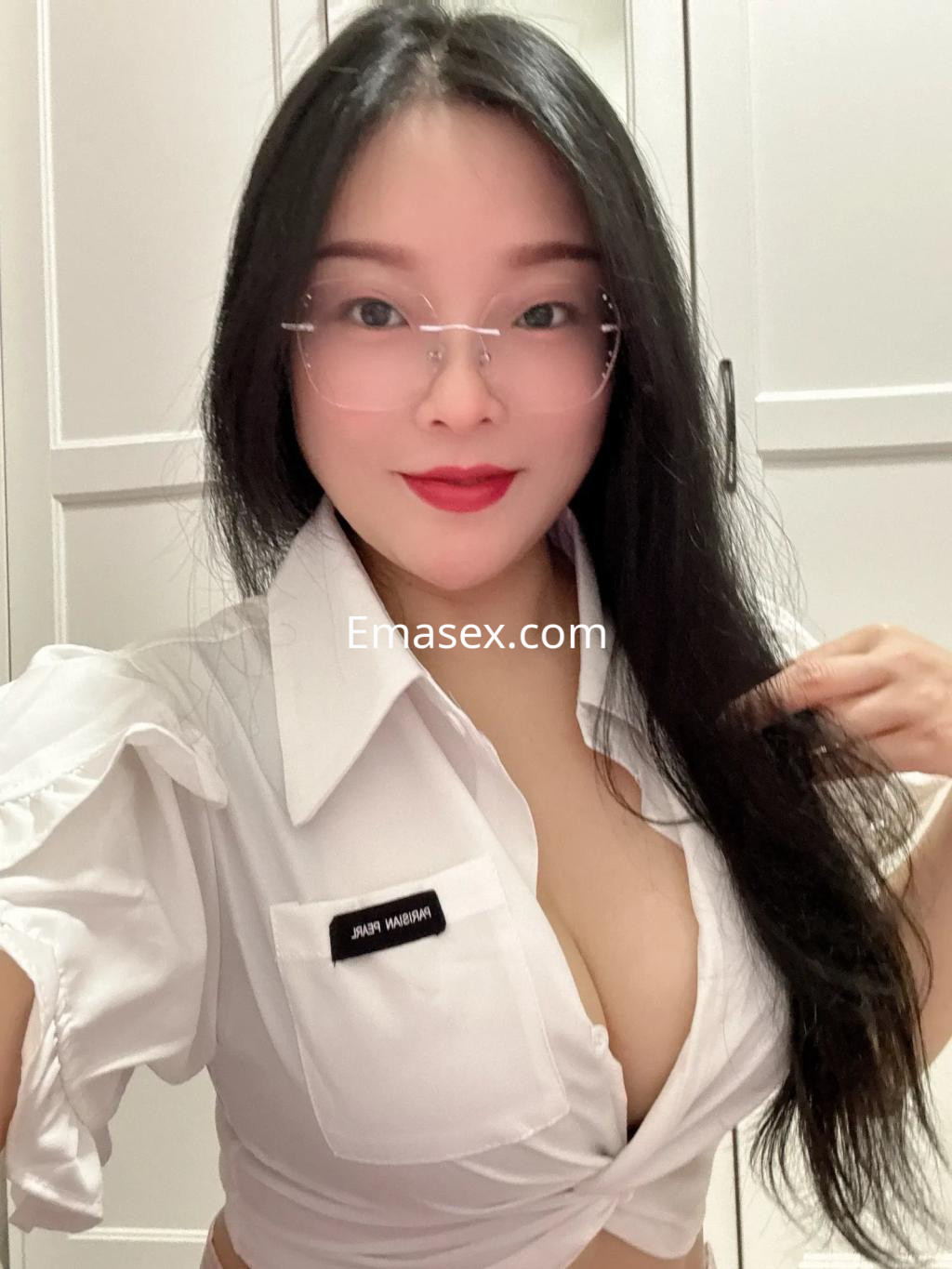 Escort en Palma de Mallorca con cabello largo y negro, usa una blusa blanca con escote y gafas.