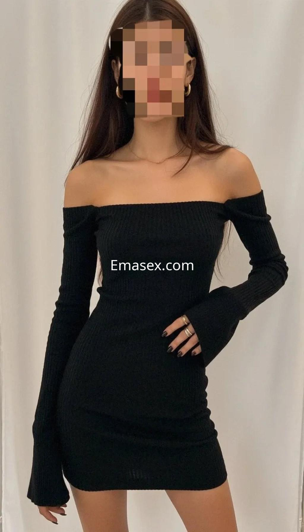 Escort en Palma de Mallorca con vestido negro ajustado de mangas largas, posando frente a fondo neutro.