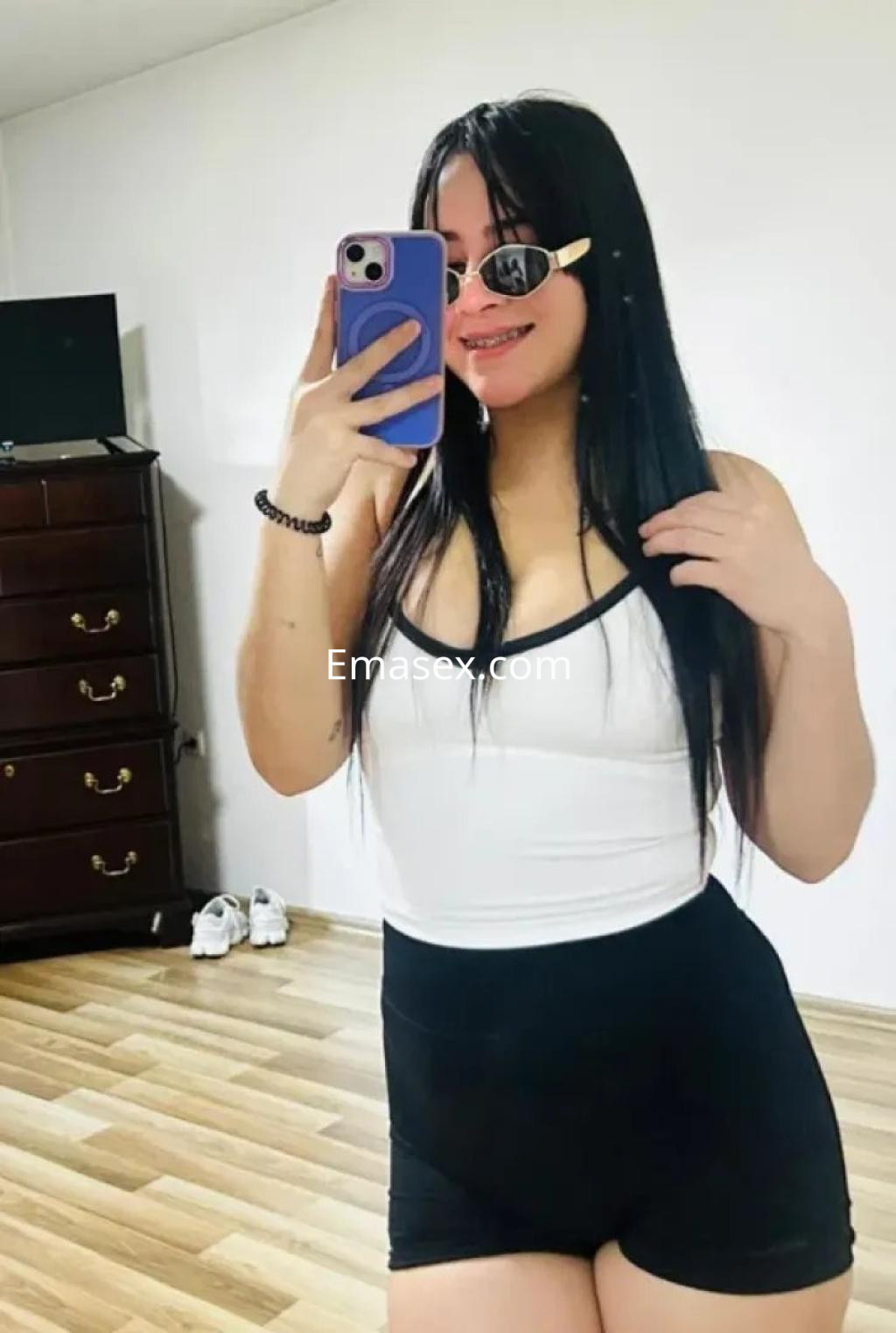 Escort en Palma de Mallorca, posando con un top blanco y pantalones cortos negros, usando gafas de sol.