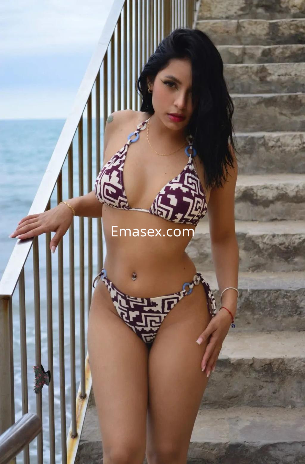 Escort en Barcelona luciendo un bikini de estampado geométrico, posando en unas escaleras junto al mar.