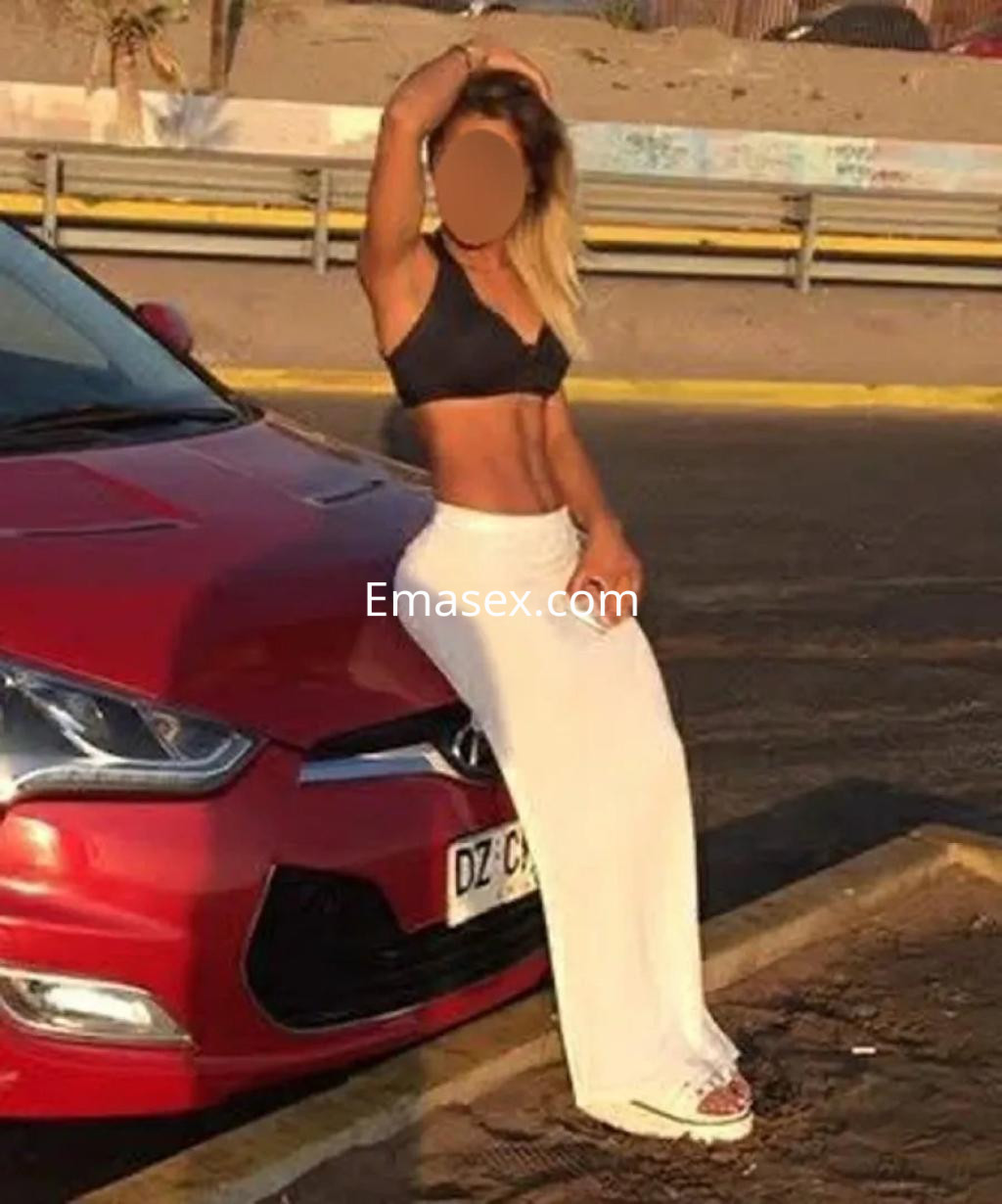 La puta posa junto a un coche rojo, luciendo un top negro y una falda blanca en Barcelona.