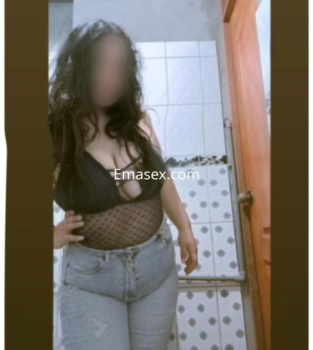 Puta en Barcelona con cabello rizado y oscuro, vistiendo un body negro y jeans ajustados en un baño.
