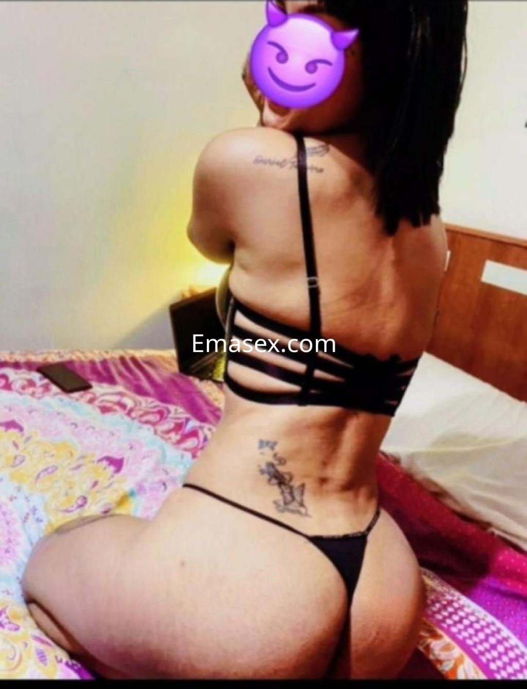 Puta de León posando de espaldas en una cama, vistiendo un conjunto de lencería negra con detalles en la espalda.