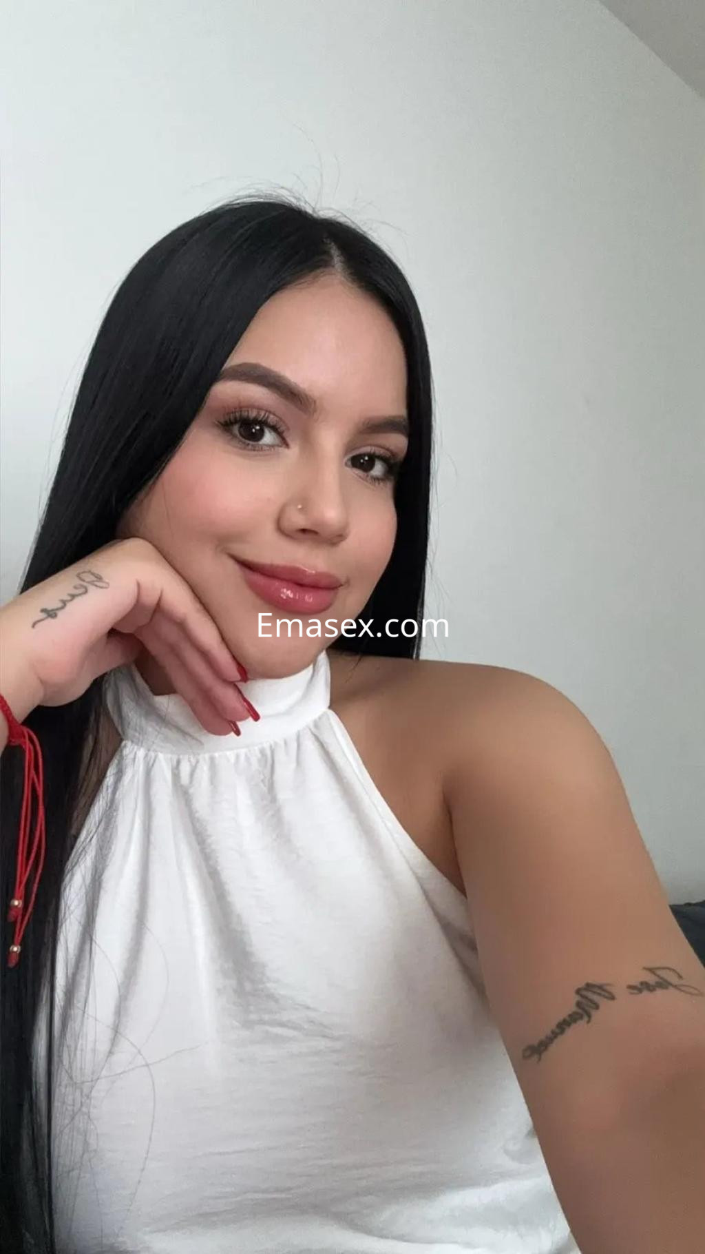 Puta en Málaga posando con una blusa blanca sin mangas, mostrando una sonrisa y un entorno minimalista.