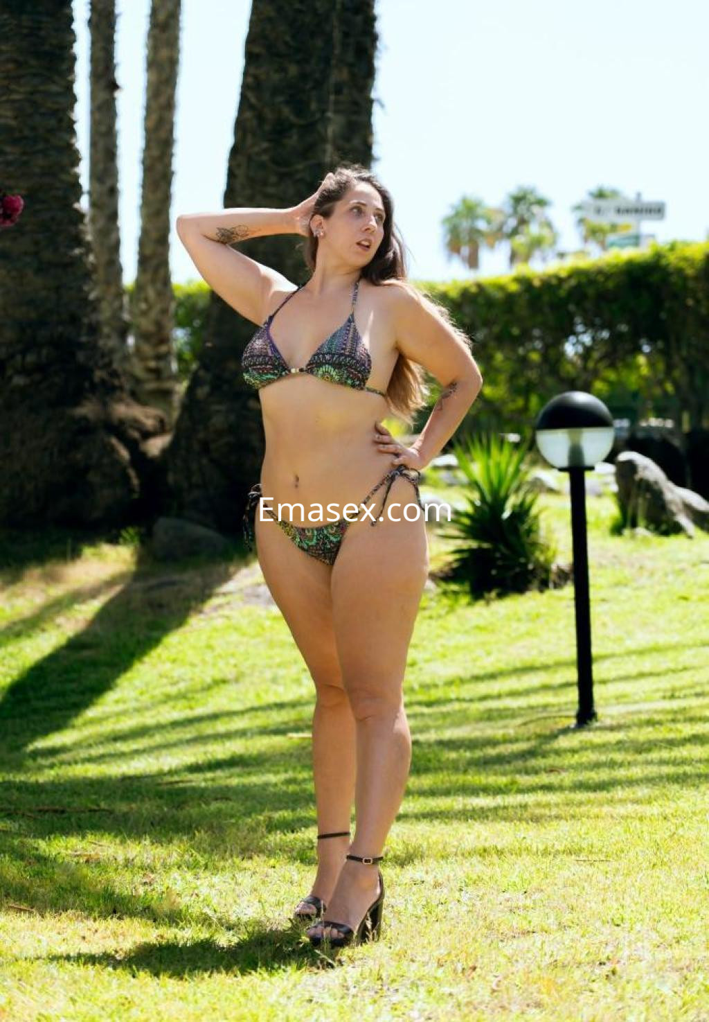 Escort en Las Palmas posando en un entorno al aire libre con bikini colorido y tacones altos.