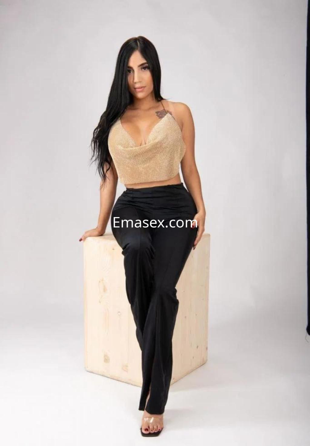Puta con cabello largo y lacio, viste un top dorado y pantalones negros, posando sentada en un cubo en Las Palmas.