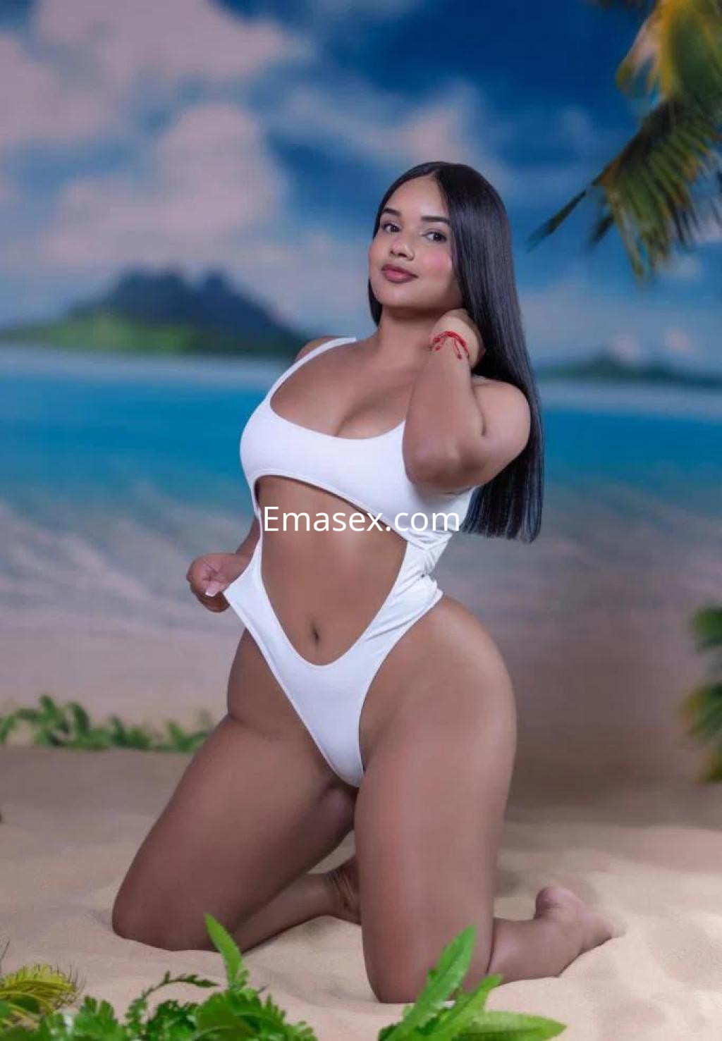 Escort con cabello largo y lacio, vestida con un traje de baño blanco, posando de rodillas en una playa de Las Palmas.