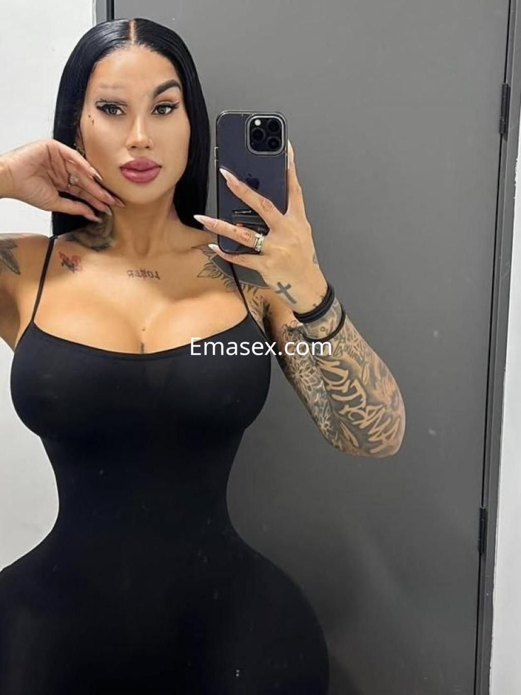 Escort en Valladolid con cabello lacio y oscuro, luciendo un vestido negro ajustado y mostrando tatuajes en los brazos.