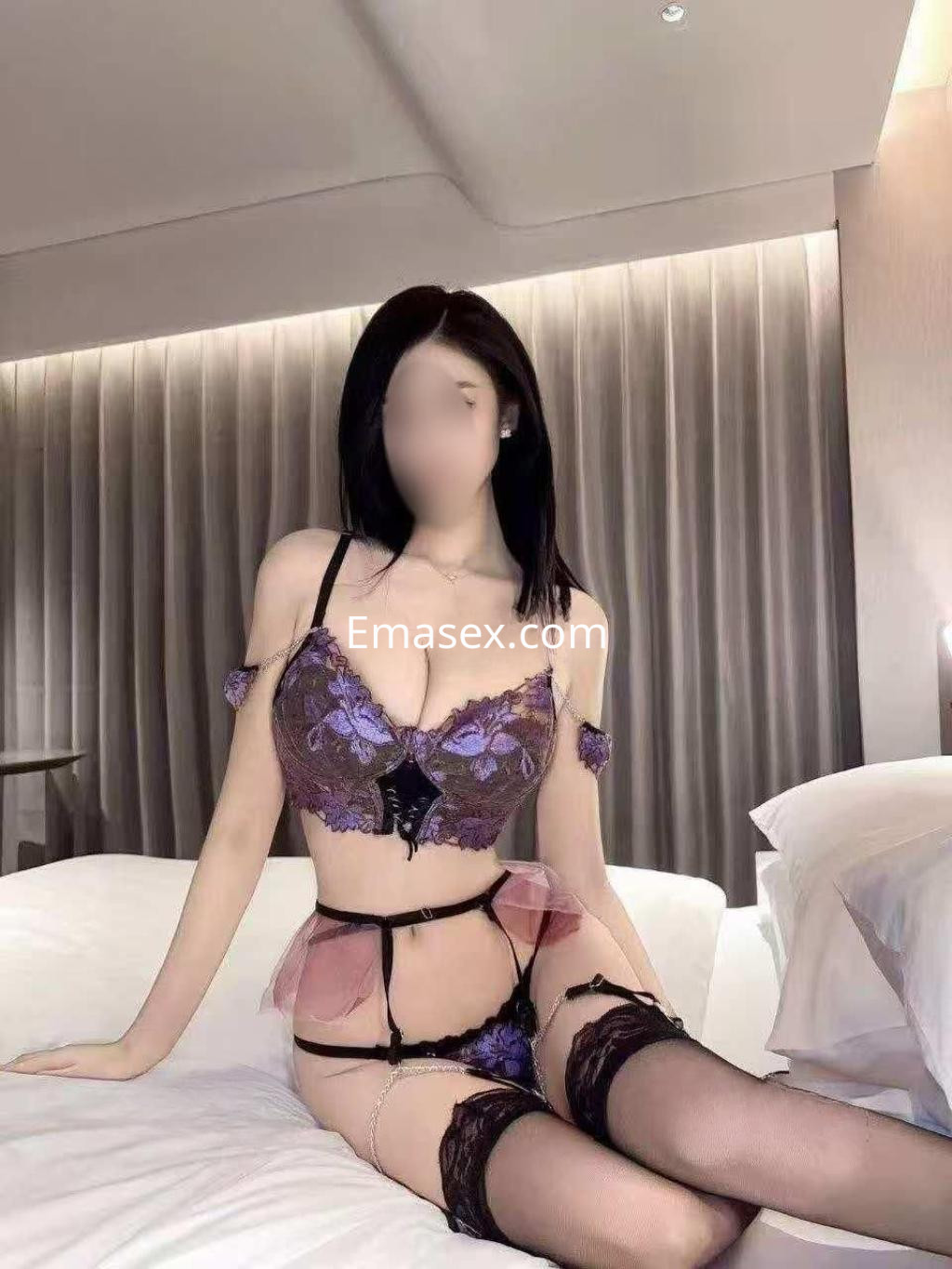 Puta en Zaragoza sentada sobre la cama, vistiendo lencería negra y púrpura con detalles de encaje.