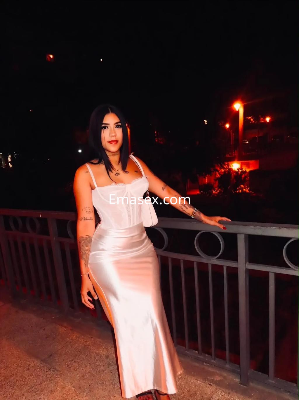 La puta lleva un vestido blanco satinado y posa junto a una barandilla en un ambiente iluminado de Zaragoza.