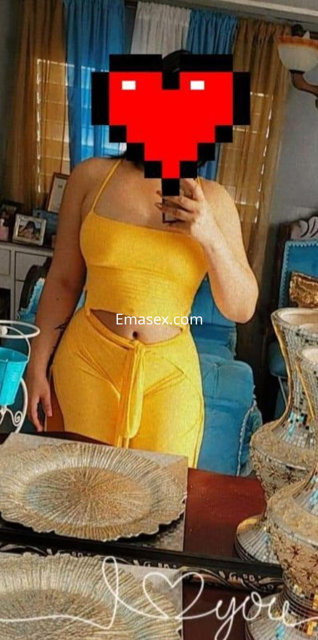 Escort en Oviedo posando frente a un espejo, vistiendo un conjunto amarillo de top y pantalones ajustados.