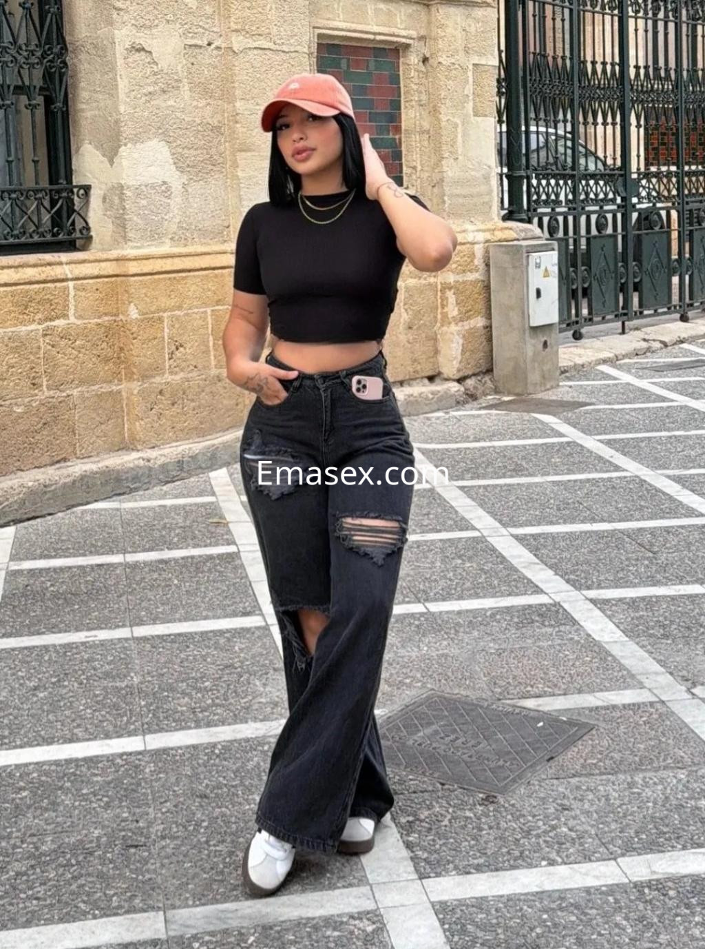 La puta en Cádiz viste una camiseta negra ajustada y jeans rasgados, complementados con una gorra.
