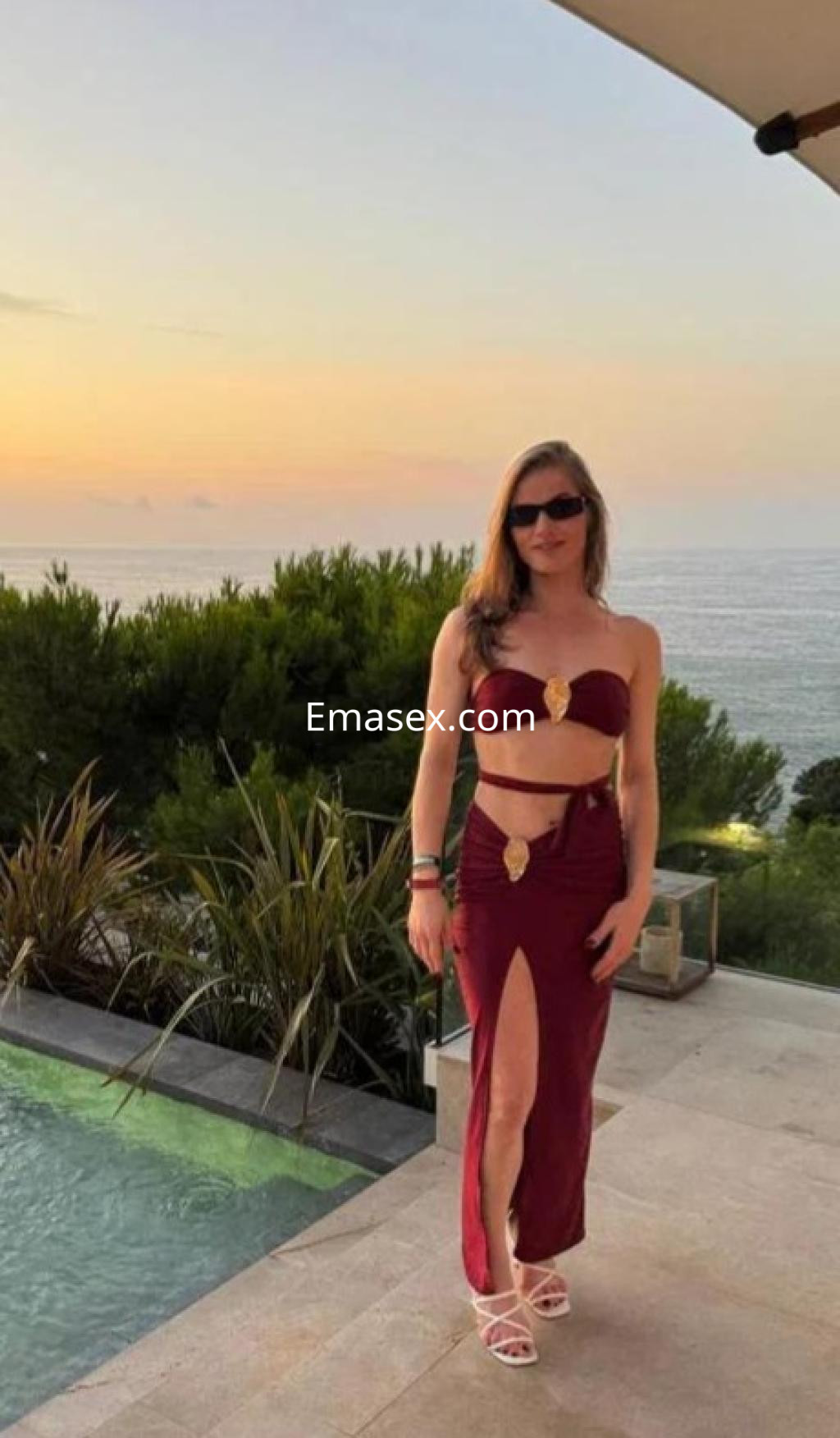 Escort en Tarragona con un conjunto de dos piezas de color burdeos, posando junto a una piscina al atardecer.
