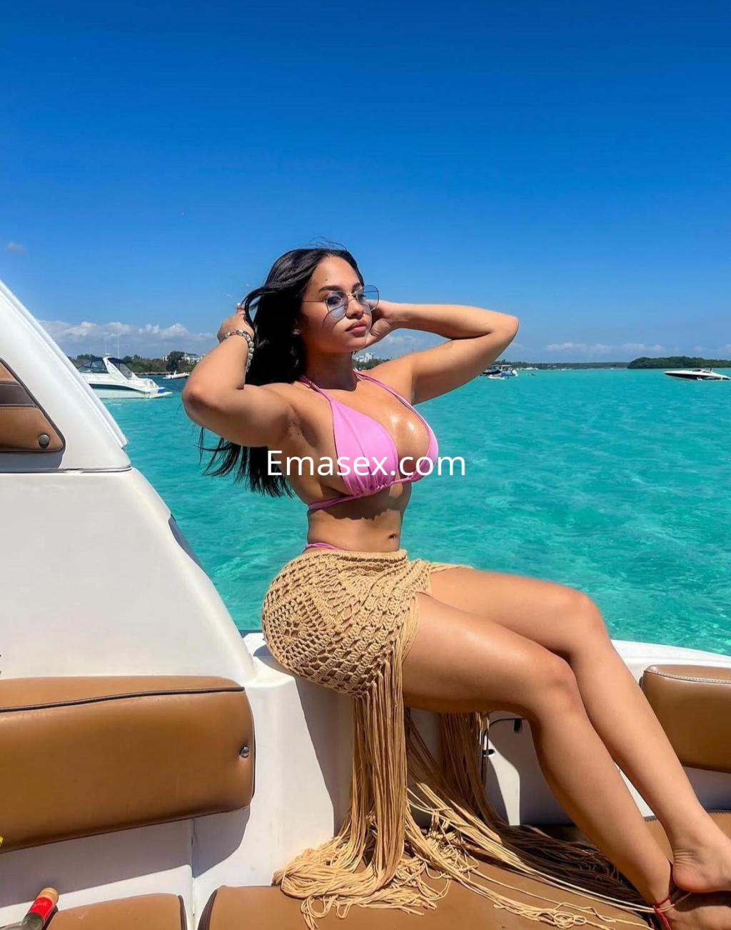 Escort en Málaga sentada en un yate, luciendo un bikini rosa y una falda de crochet, disfrutando del sol.