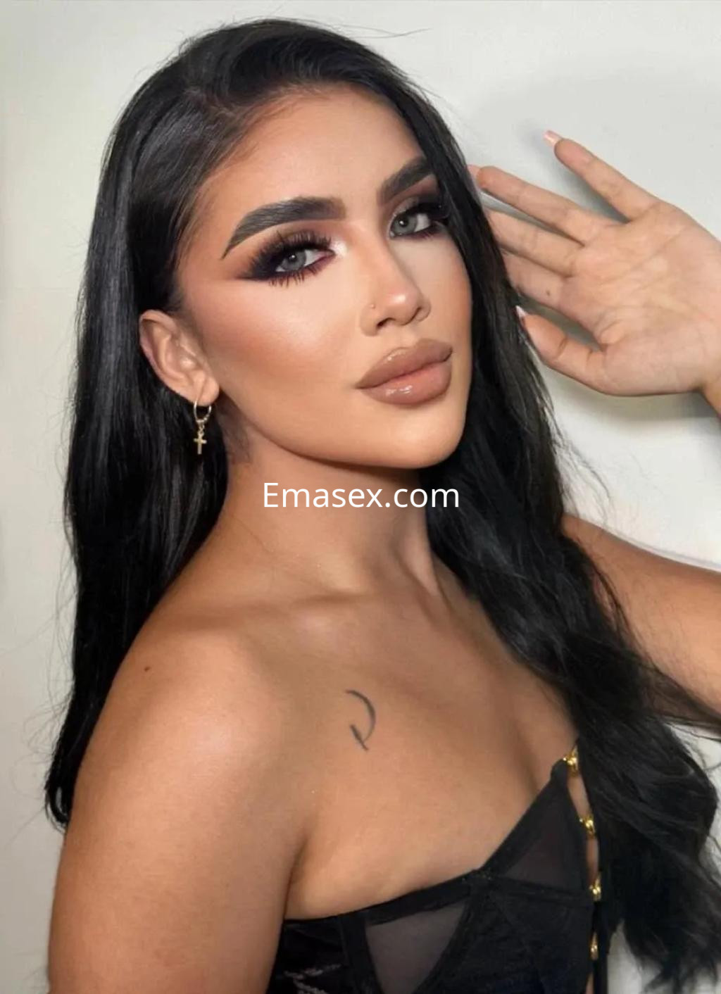 Escort en Albacete con cabello largo y lacio, maquillaje destacado y atuendo ligero, posando con una mano en la cara.