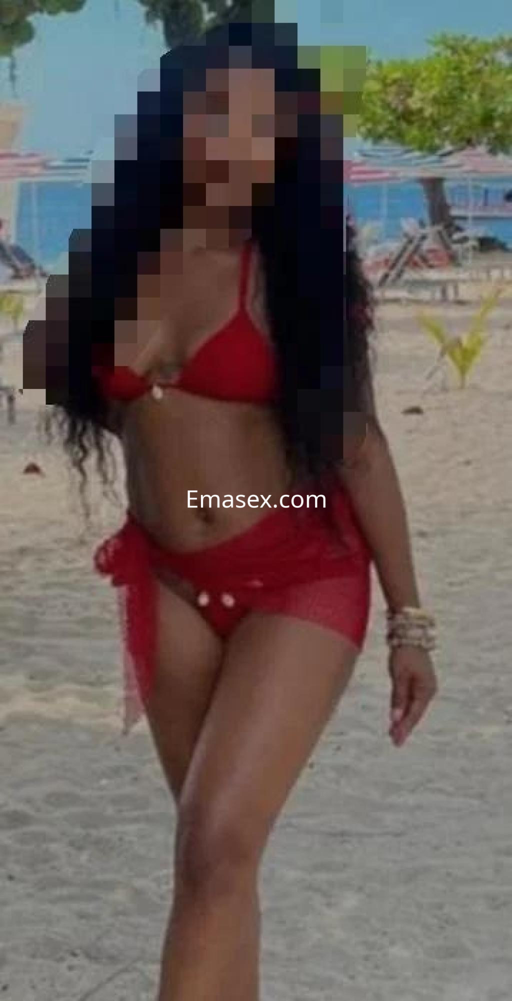 Escort en Badajoz con cabello largo y rizado, vistiendo un bikini rojo y pareo en la playa.