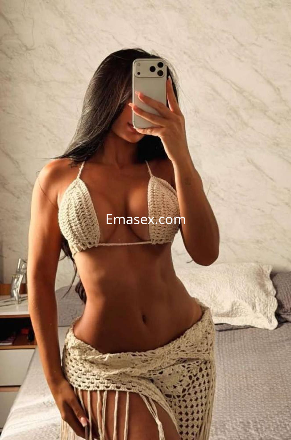Escort en Ibiza posando con un bikini de crochet beige, mostrando su figura esbelta frente al espejo.