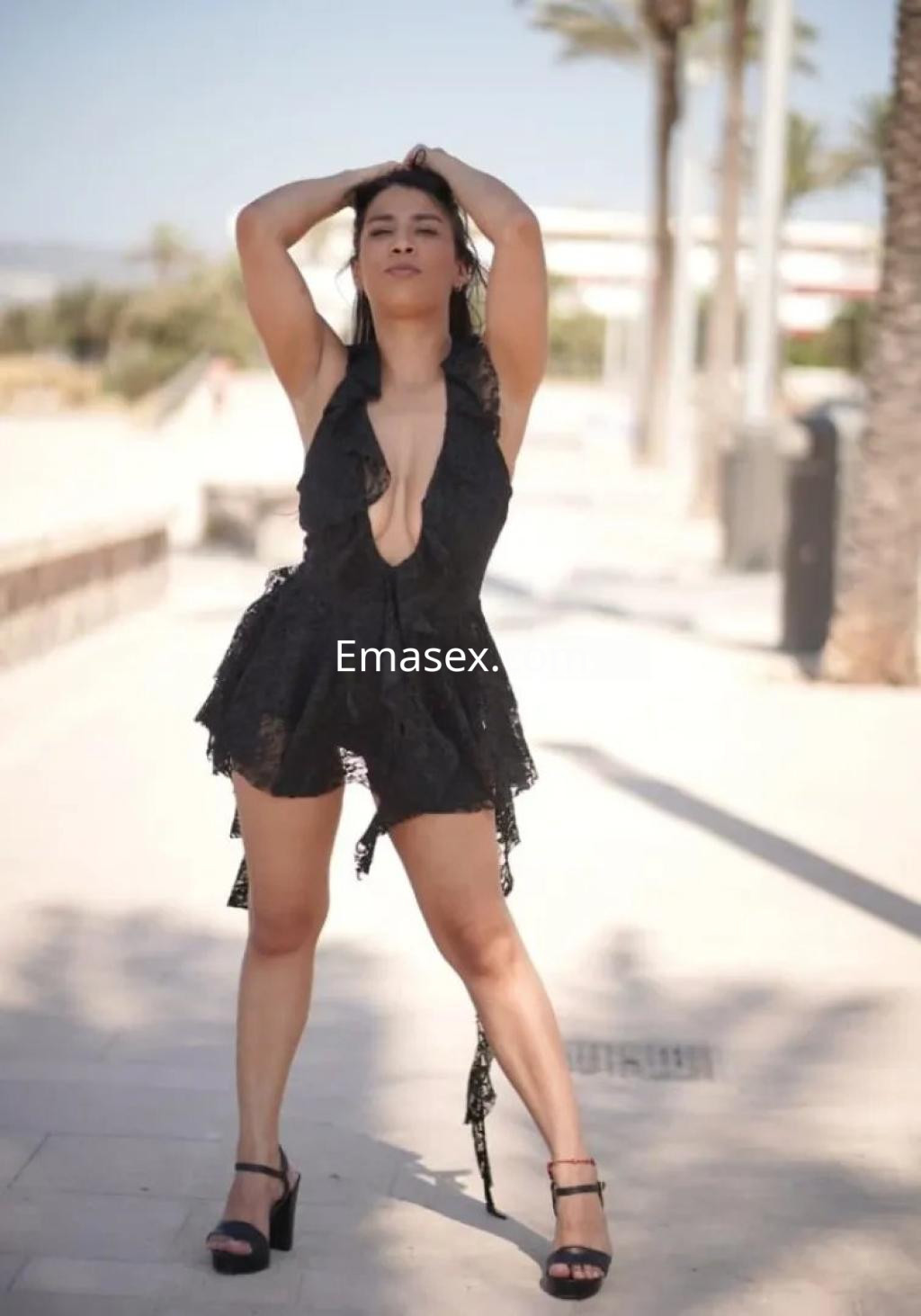 Escort en Palma de Mallorca luciendo un vestido negro con detalles de encaje y sandalias, posando en la calle.
