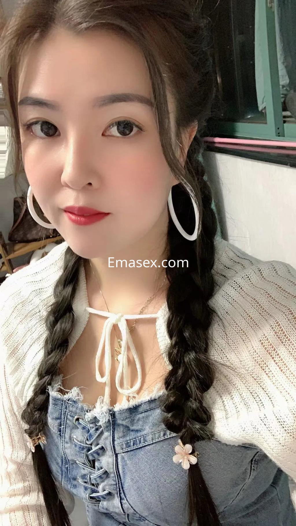 Escort en Palma de Mallorca con trenzas y blusa blanca, posando con un collar delicado y pendientes grandes.
