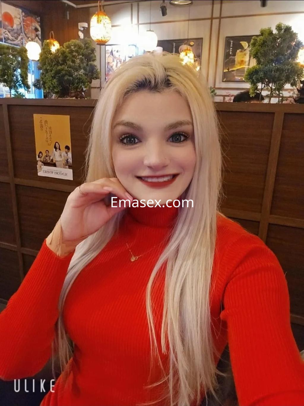 Puta con cabello largo y rubio, vistiendo un suéter rojo, sonríe mientras posa en un restaurante en Córdoba.