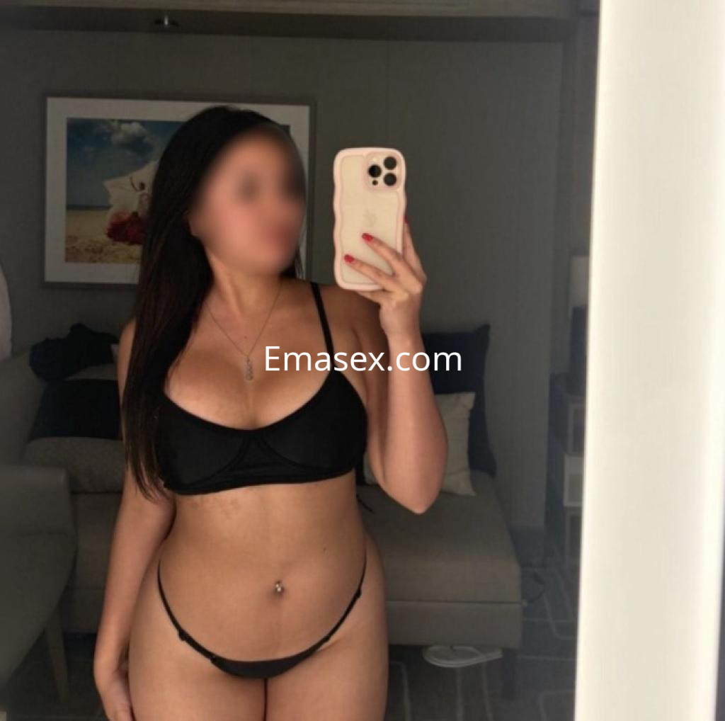 Escort en Lleida se muestra en un espejo con un bikini negro, posando con el pelo largo y lacio.