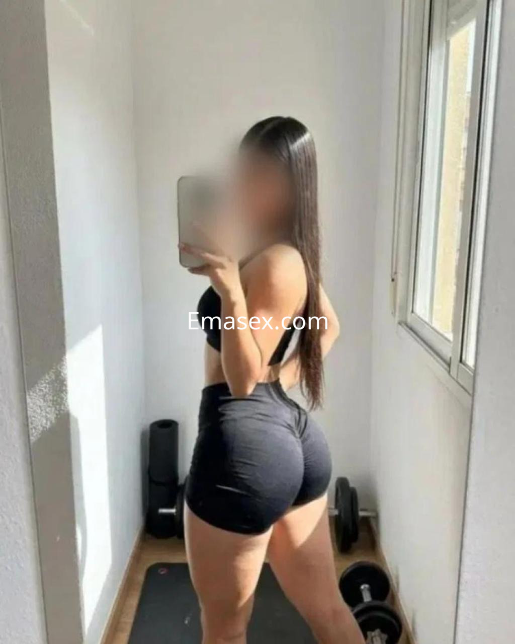 Puta de Lugo en una pose de perfil, viste un top negro y shorts ajustados en un ambiente de gimnasio.