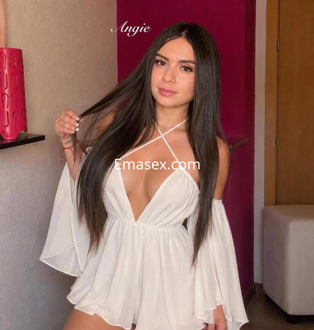 La puta luce un conjunto blanco con mangas largas y un escote pronunciado, posando en un ambiente interior en Madrid.