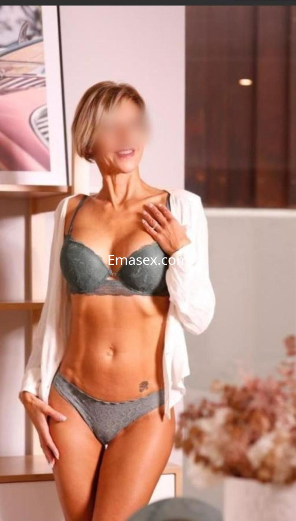 Escort en Pontevedra, posando con lencería gris y una camisa blanca, en un ambiente moderno y acogedor.