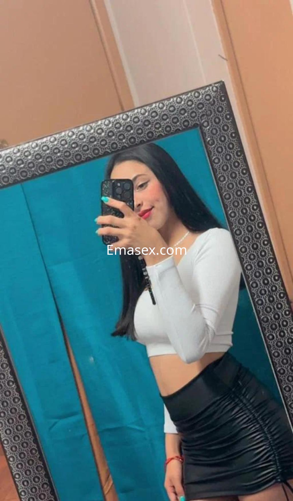 La puta en Toledo lleva un top blanco y una falda negra ajustada, posando frente a un espejo.