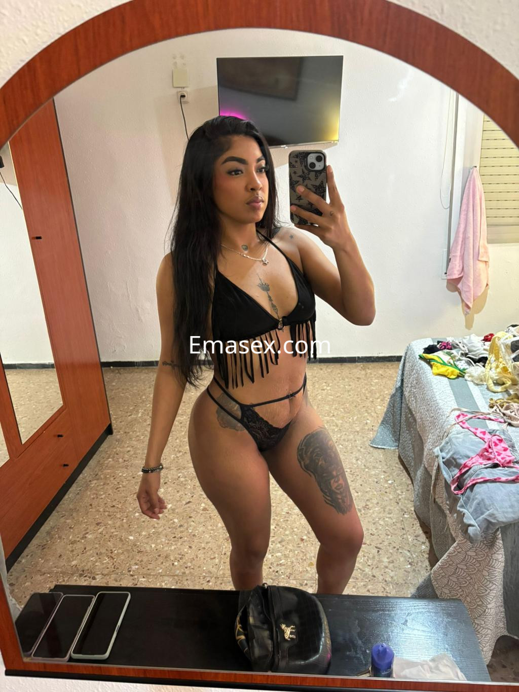Escort en Bilbao posando frente a un espejo, con un bikini negro con flecos y un tatuaje visible en la pierna.